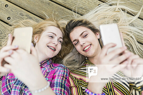 Happy teenagers taking selfie through smart phone lying on floorboard