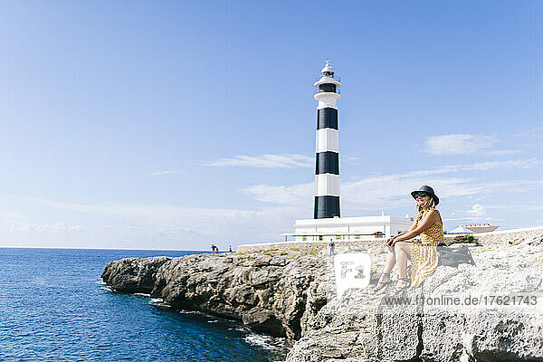 Woman sitting on rock by sea at Artrutx Lighthouse in Minorca  Spain