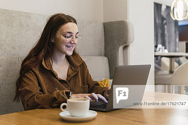 Smiling businesswoman working on laptop in coffee shop