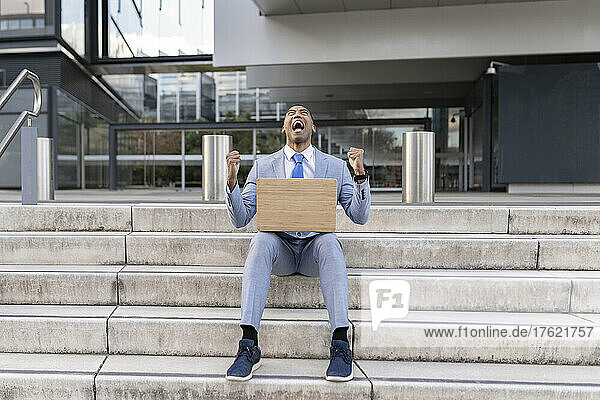 Screaming businessman with laptop gesturing fists sitting on steps