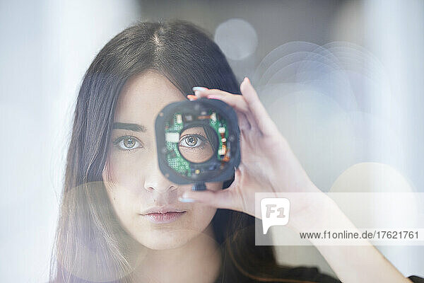 Young woman looking through open camera lens at office