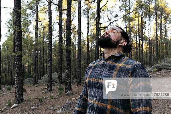 Bärtiger Mann mit geschlossenen Augen steht im Wald