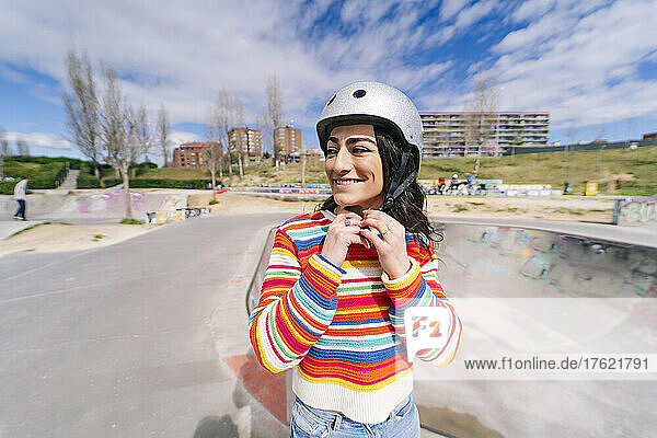 Smiling woman adjusting helmet in skateboard park