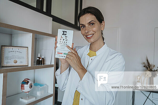 Smiling doctor pointing at eye chart in clinic