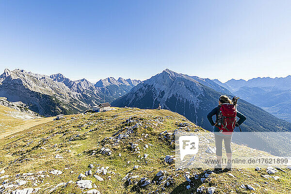 Female hiker admiring surrounding landscape from mountaintop with Tiroler Hutte retreat in background