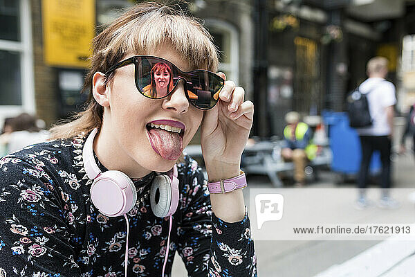 Frau mit Sonnenbrille streckt auf der Straße die Zunge heraus