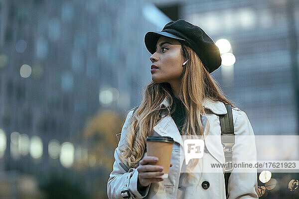 Blond woman wearing cap holding disposable coffee cup