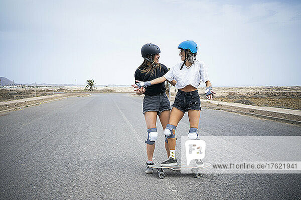 Young woman teaching skateboarding to friend on road