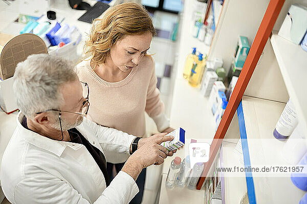 Pharmacist helping customer reading instruction on medicine box at pharmacy store