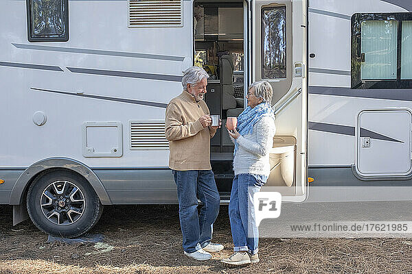 Senior couple with coffee cup standing by motor home
