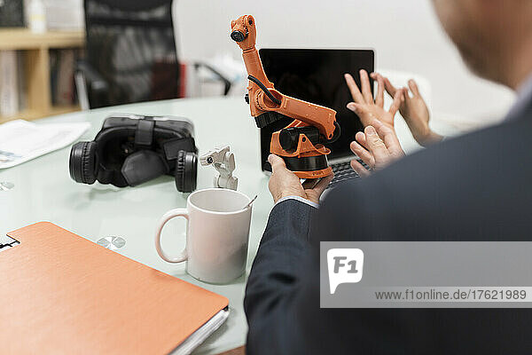Businessman discussing robotic arm with colleague at desk