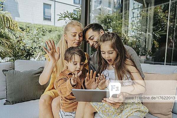 Family waving on video call through tablet PC at patio