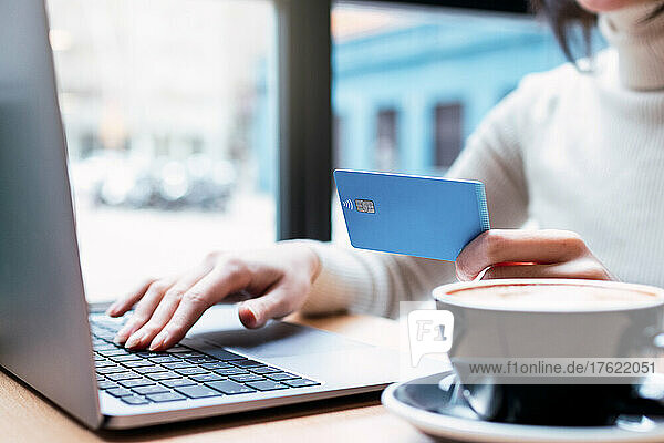 Businesswoman holding credit card doing online shopping through laptop at cafe