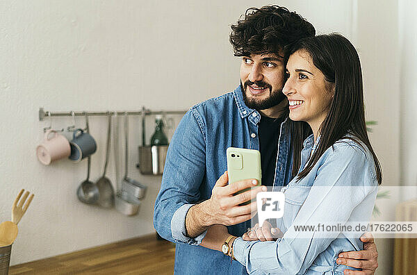 Lächelndes Paar macht Selfie per Smartphone in der heimischen Küche