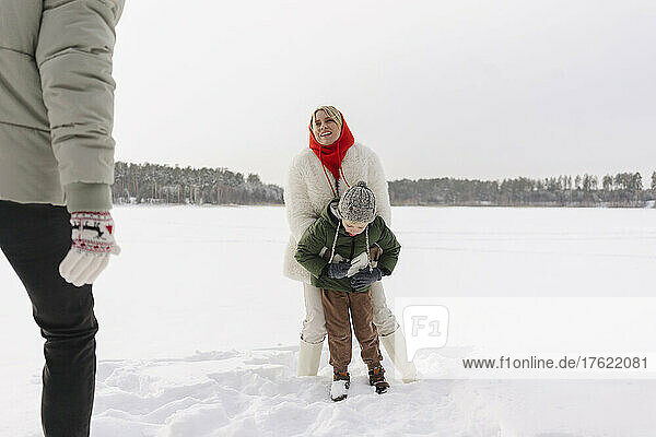 Smiling woman embracing son looking at man standing on snow