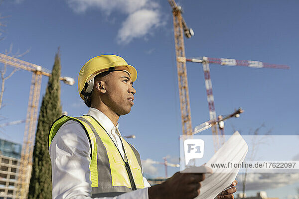 Architect holding blueprint working at construction site on sunny day