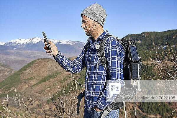Mann steht mit der Hand in der Tasche und checkt an einem sonnigen Tag sein Smartphone