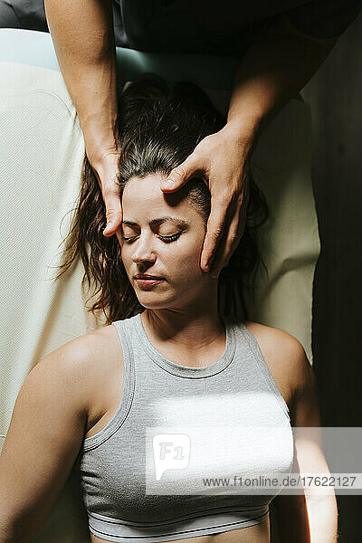 Physiotherapist giving head massage to woman lying with eyes closed
