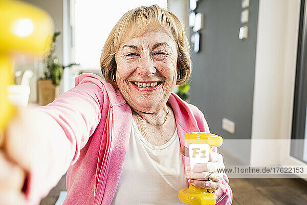 Cheerful senior woman working out with yellow dumbbells at home