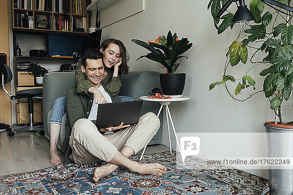 Happy young couple sharing laptop in living room at home
