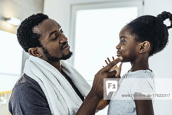 Father applying moisturizer to daughter in bathroom
