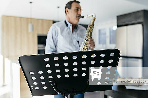 Saxophonist practicing saxophone in front of musical stand at home