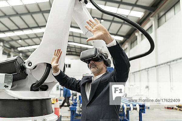 Businessman wearing virtual reality simulator standing with arms raised in factory