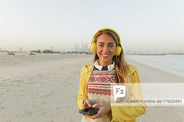 Happy woman on beach with wireless headphones listening to music