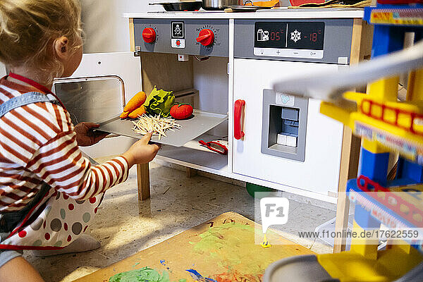 Son putting vegetables tray by oven in toy kitchen at home