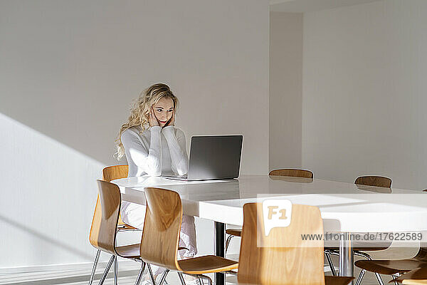 Blond freelancer with head in hand sitting looking at laptop