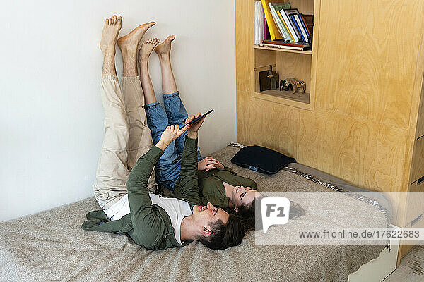 Smiling young couple sharing tablet PC lying on bed at home