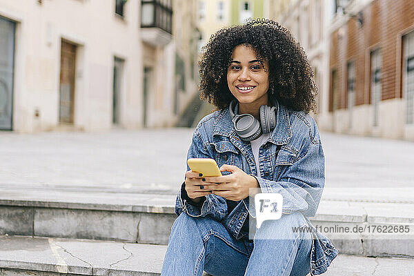 Smiling woman with smart phone and headphones on steps