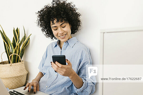 Smiling young woman with laptop and smart phone sitting at home