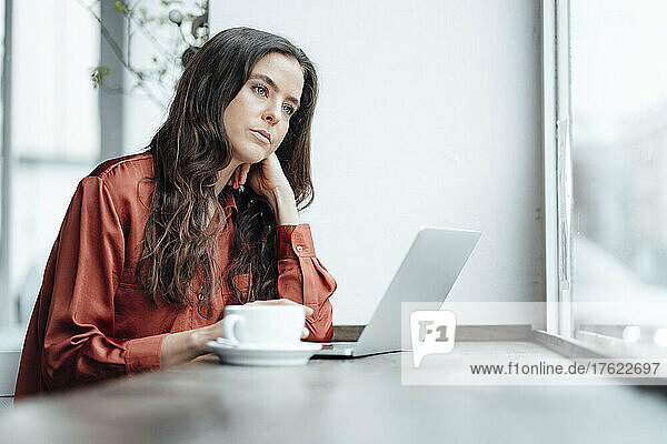 Contemplative woman with laptop in cafe