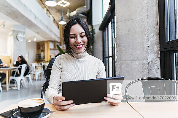 Happy woman holding tablet PC sitting at cafe