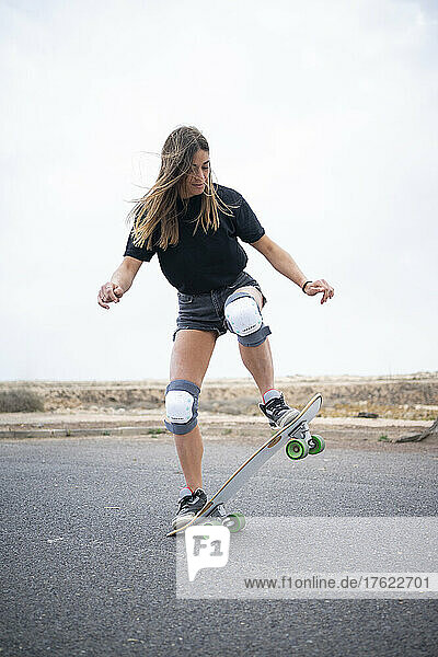 Young woman showing skill with skateboard on road