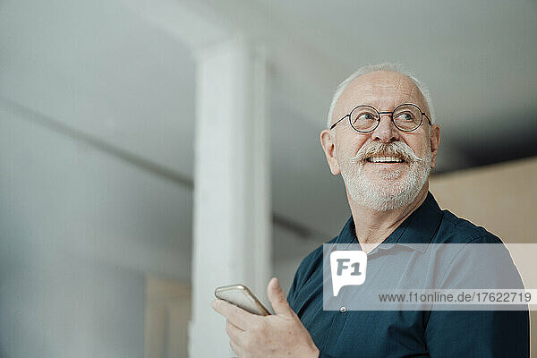 Happy senior man holding smart phone in office