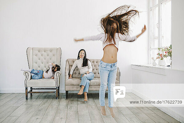 Girl jumping with mother and daughter in background at home