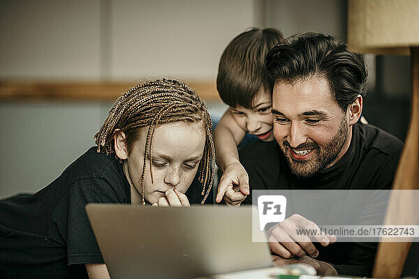 Boy pointing on laptop to father and brother at home