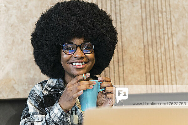 Smiling woman with eyeglasses holding mug in coffee shop