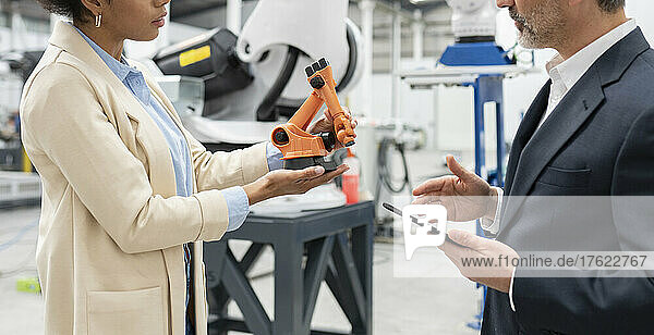 Developer showing model of robotic arm to businessman in factory