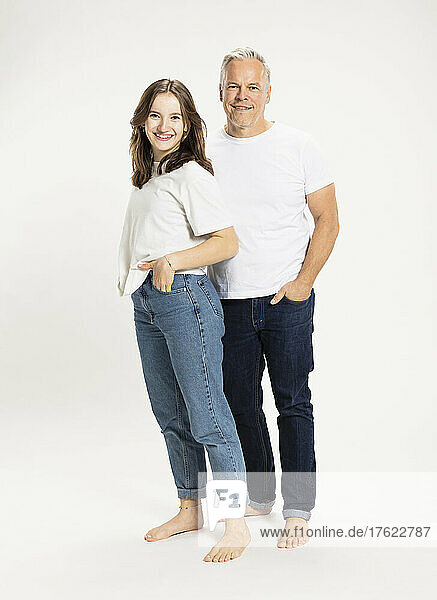 Happy father and daughter standing with hands in pockets at studio