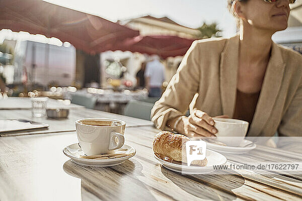 Frau hält Kaffeetasse in der Hand und sitzt an einem sonnigen Tag im Straßencafé