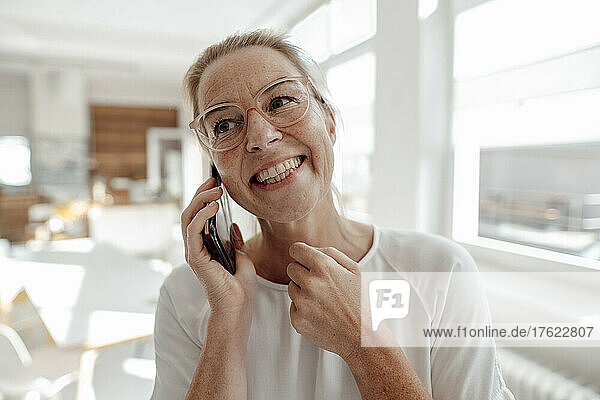 Glückliche Geschäftsfrau  die im Büro auf dem Smartphone spricht