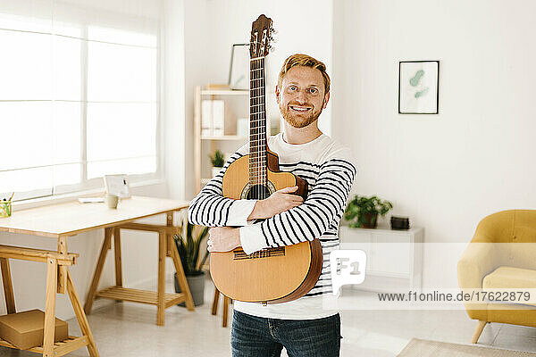 Happy young man with guitar standing in living room at home