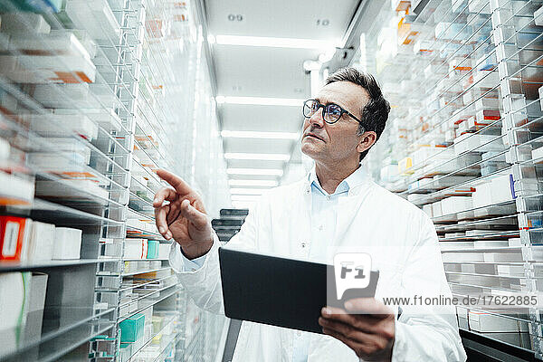 Pharmacist with tablet PC checking medicines on rack and taking inventory in storage room