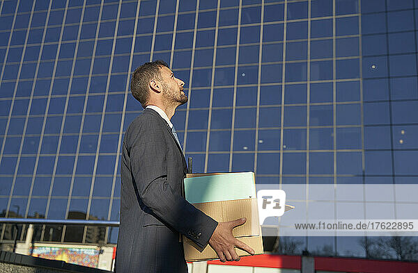 Businessman carrying box by office building on sunny day