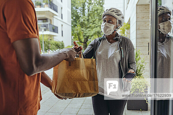 Woman with protective face mask delivering food bag to man at doorway