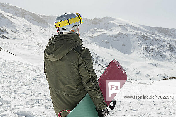 Young man with snowboard standing on snowcapped mountain