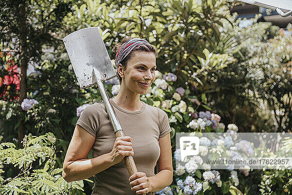 Smiling gardener holding shovel in garden